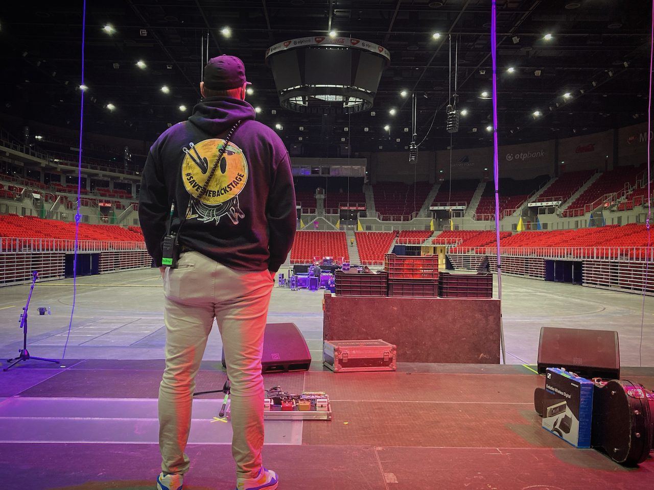 On stage in an empty arena before doors, wearing a #SaveTheBackstage hoodie