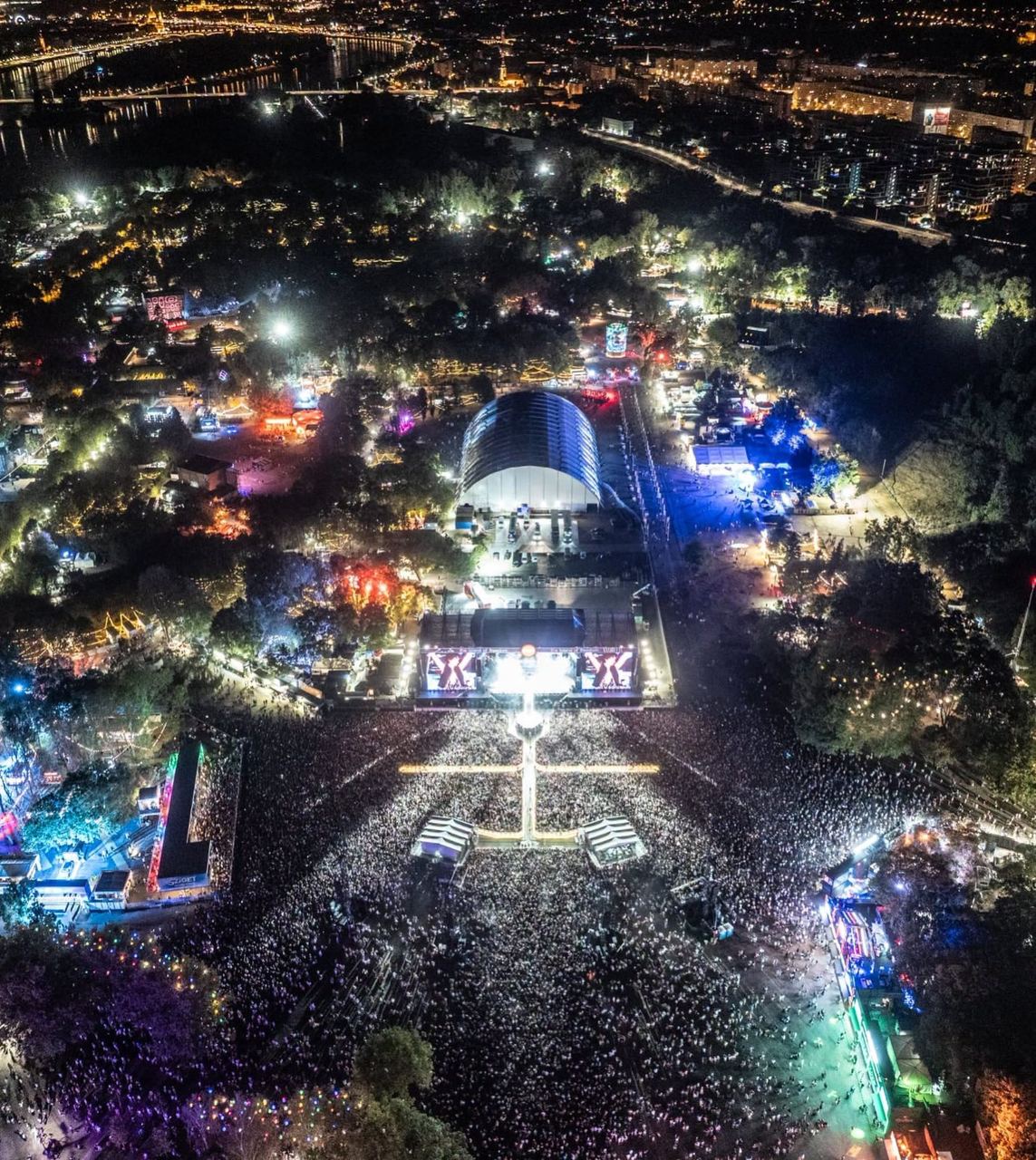 Aerial night view of a festival main stage and crowd beside the Danube